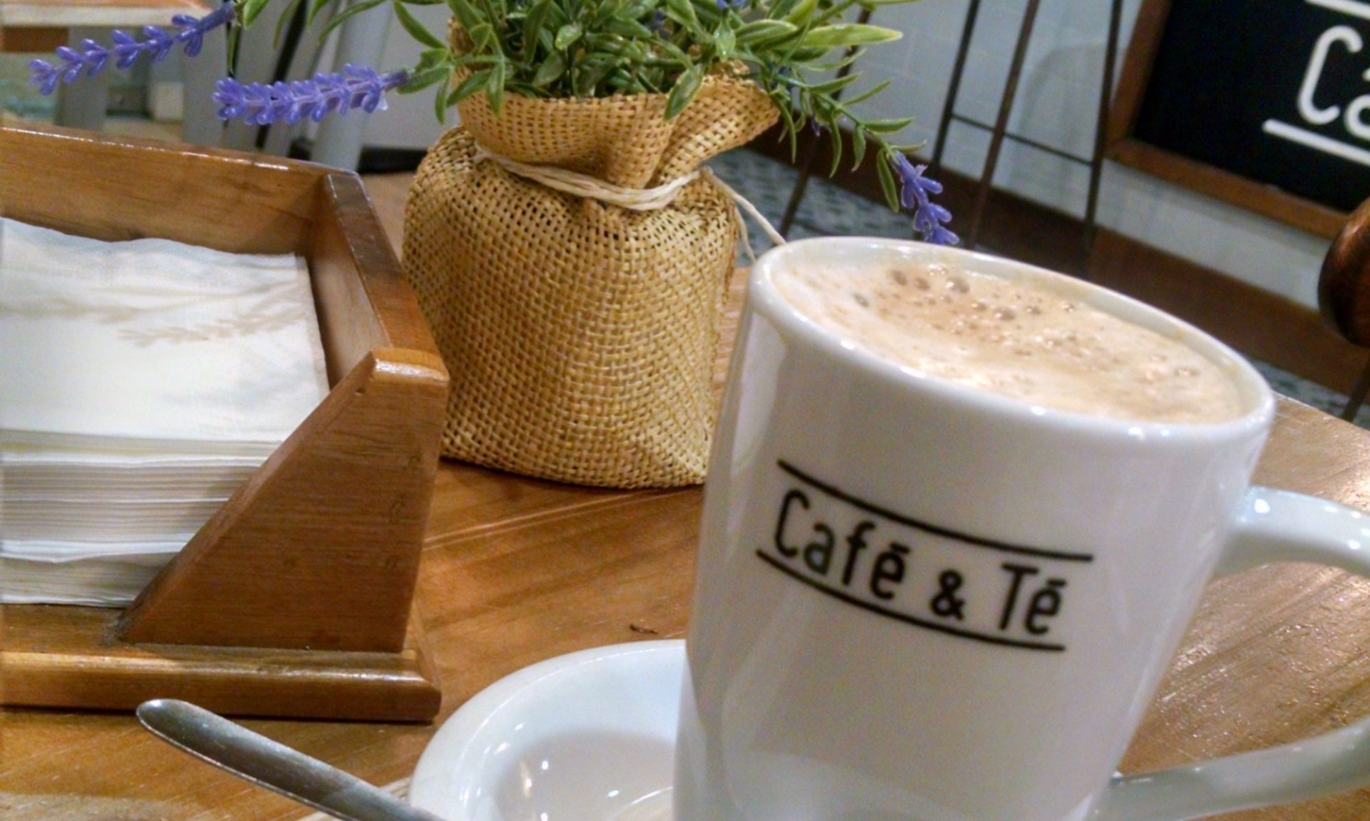 Fancy mug of a tea latte from a cafe in Madrid (called Cafe a Te) from my trip in 2017. It's close focus on a cute cup and saucer on a wood table with a cute little table plant in the background